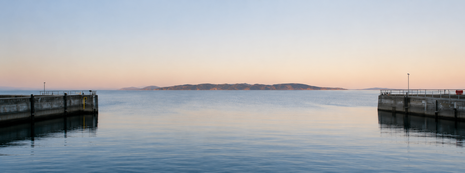 A quiet coastal harbor at dawn with mist over still water.